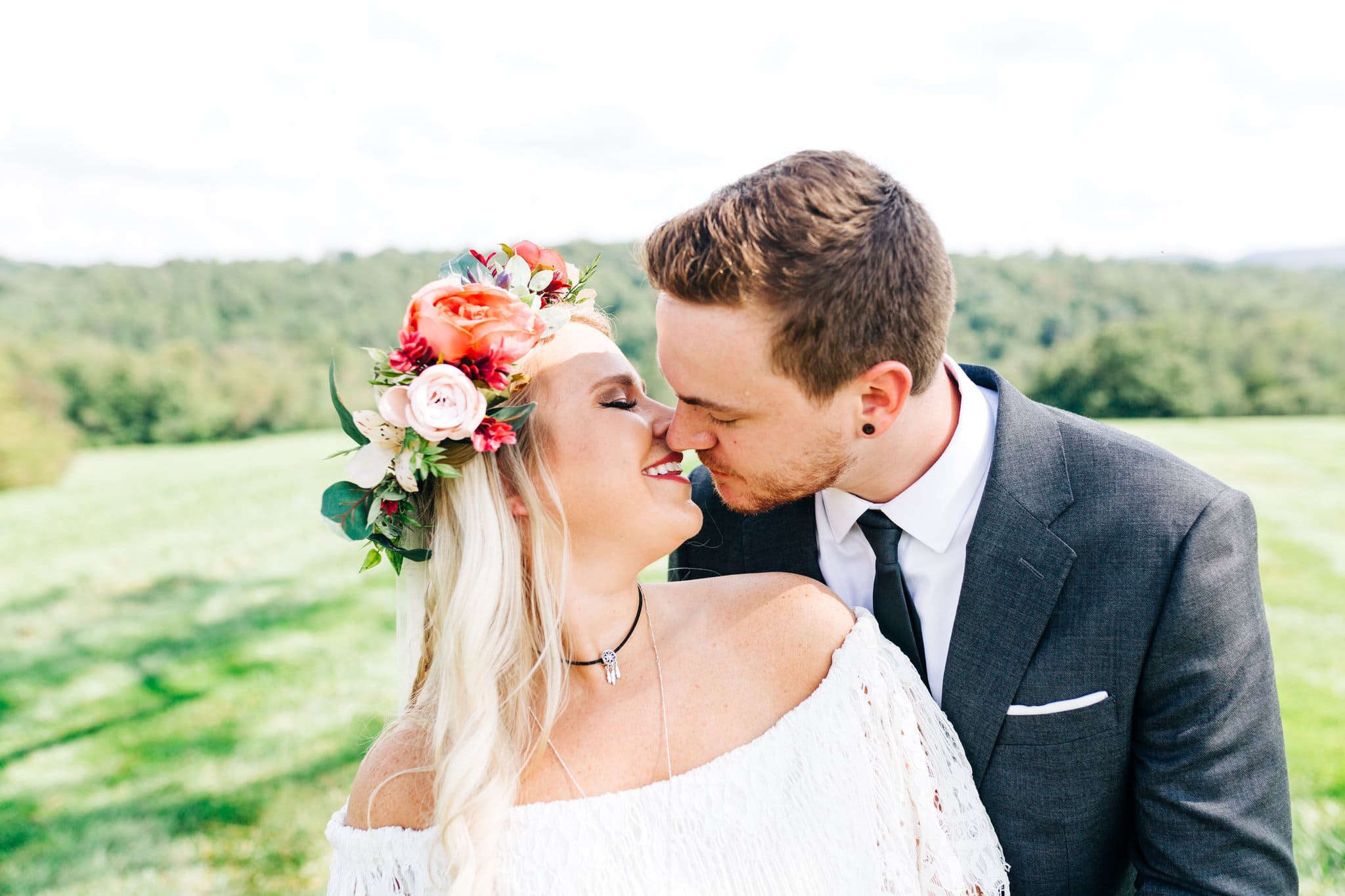 bride with white off shoulder lace dress with pink and white flower crown kissing groom with grey suit with mountain views at Boho Gambill Estate Wedding 