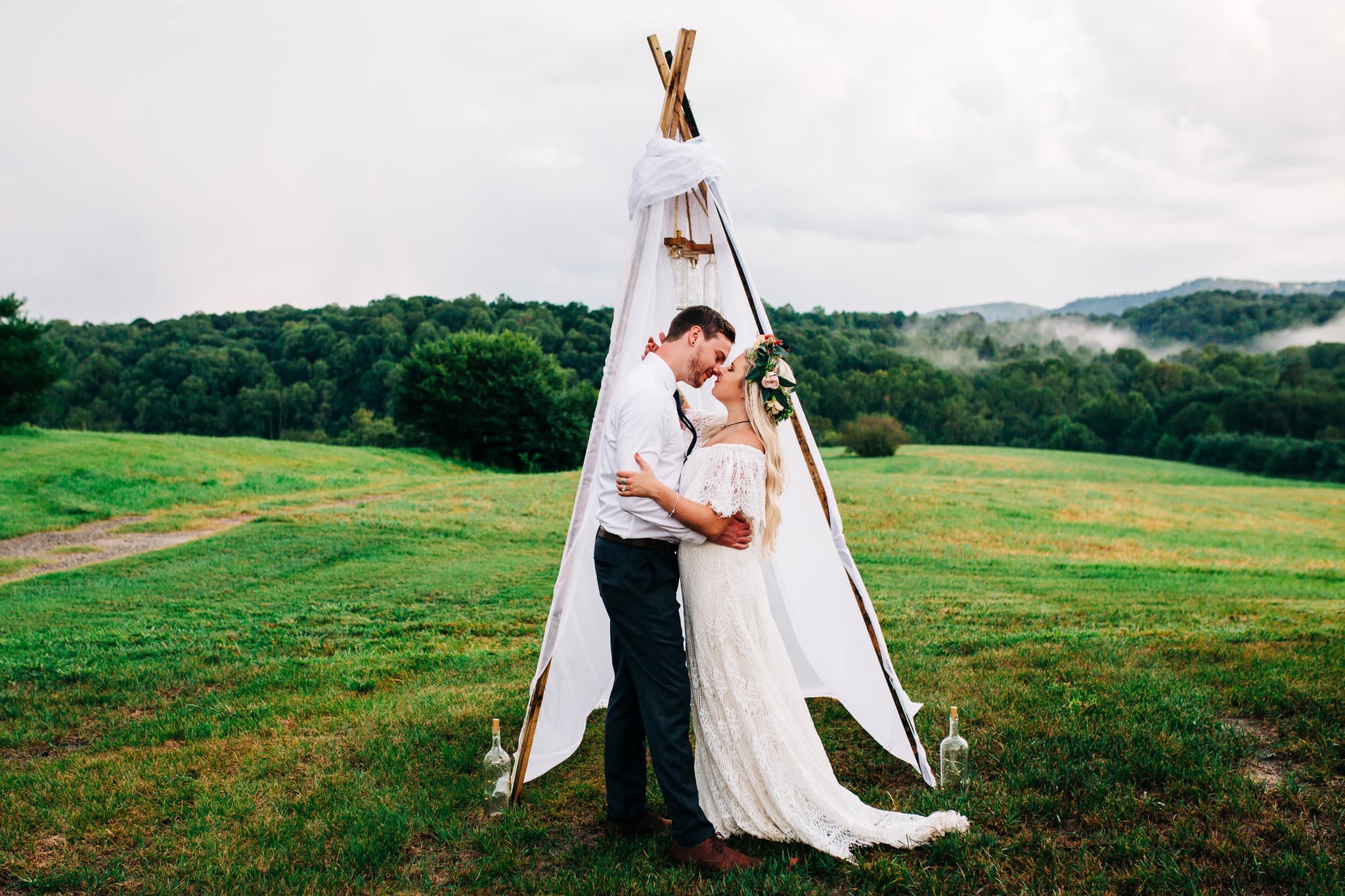 white tent with macrame with bride with lace dress with flower crown with groom with white shirt kissing with mountain views in background at Boho Gambill Estate Wedding 
