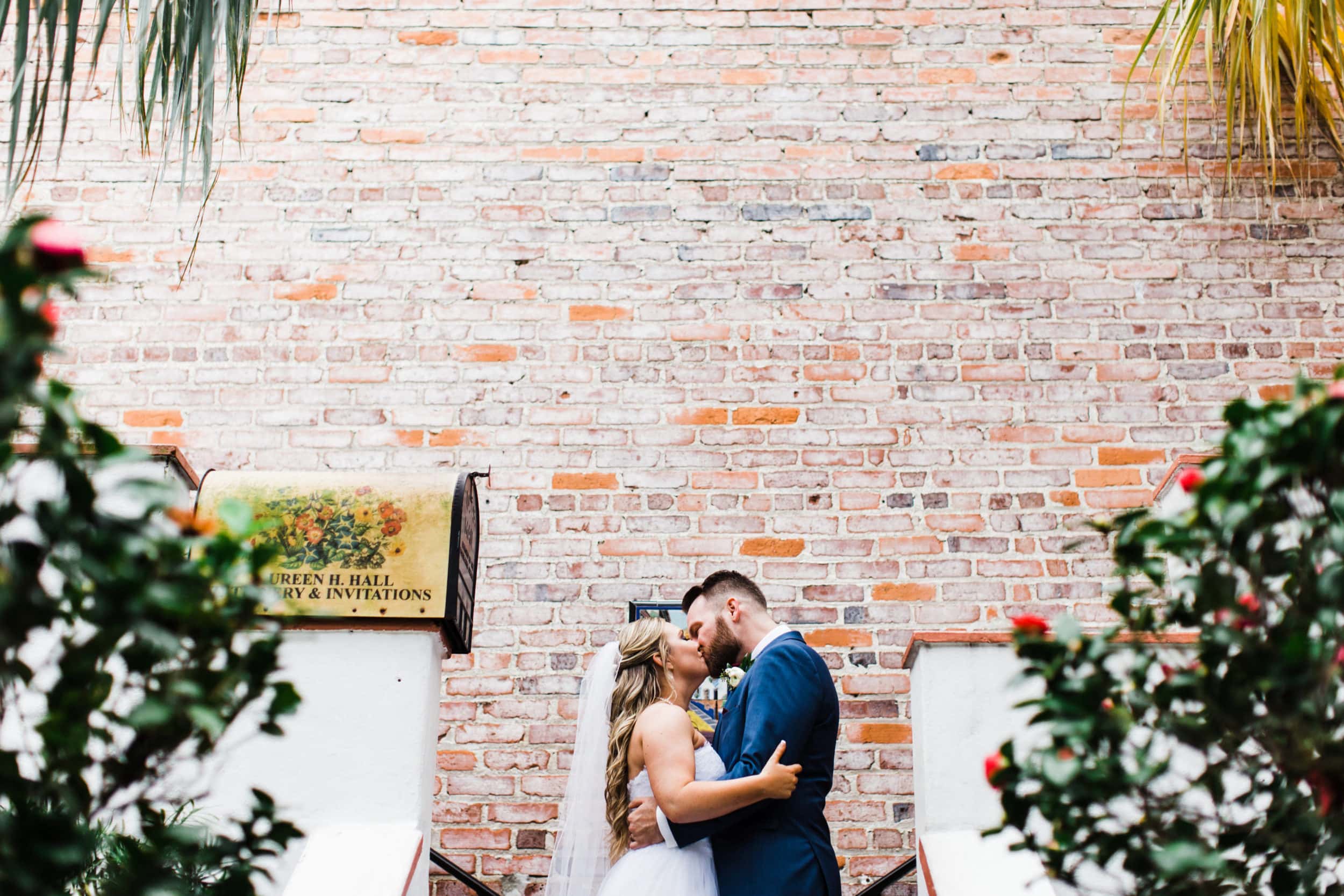 bride with groom with navy blue suit with large brick wall with country style mailbox with greenery in background at Winter Park Farmers Market Wedding