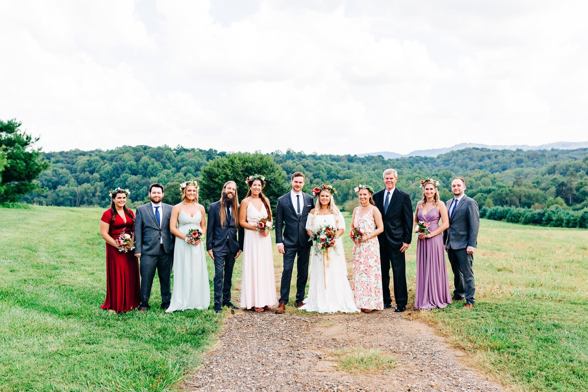bridesmaids with red, mint, purple, blush color dresses with groomsmen with grey suits with bride and groom with pink and white flowers with mountain view in background atBoho Gambill Estate Wedding 