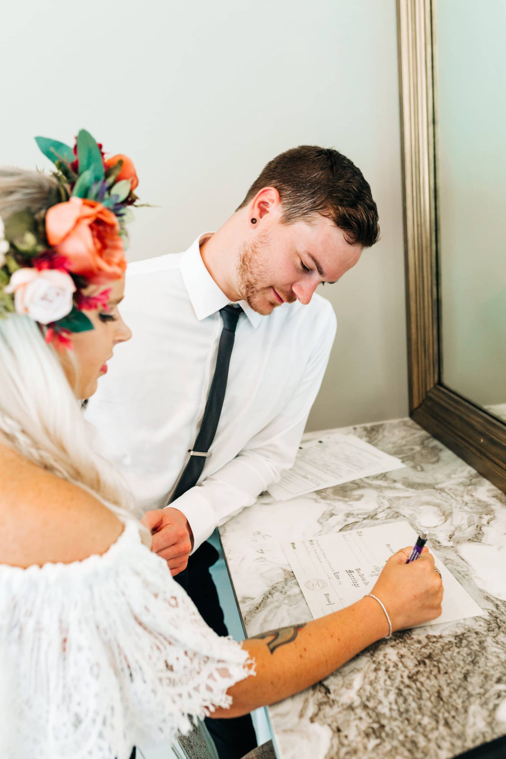 bride with lace off shoulder dress with flower crown with groom with white shirt with navy tie signing paper at Boho Gambill Estate Wedding 