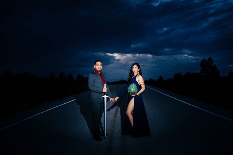 bride to be with long navy dress with green dragon egg with groom to be with sword on road with stormy sky in background at Lake Louisa State Park Engagement Session