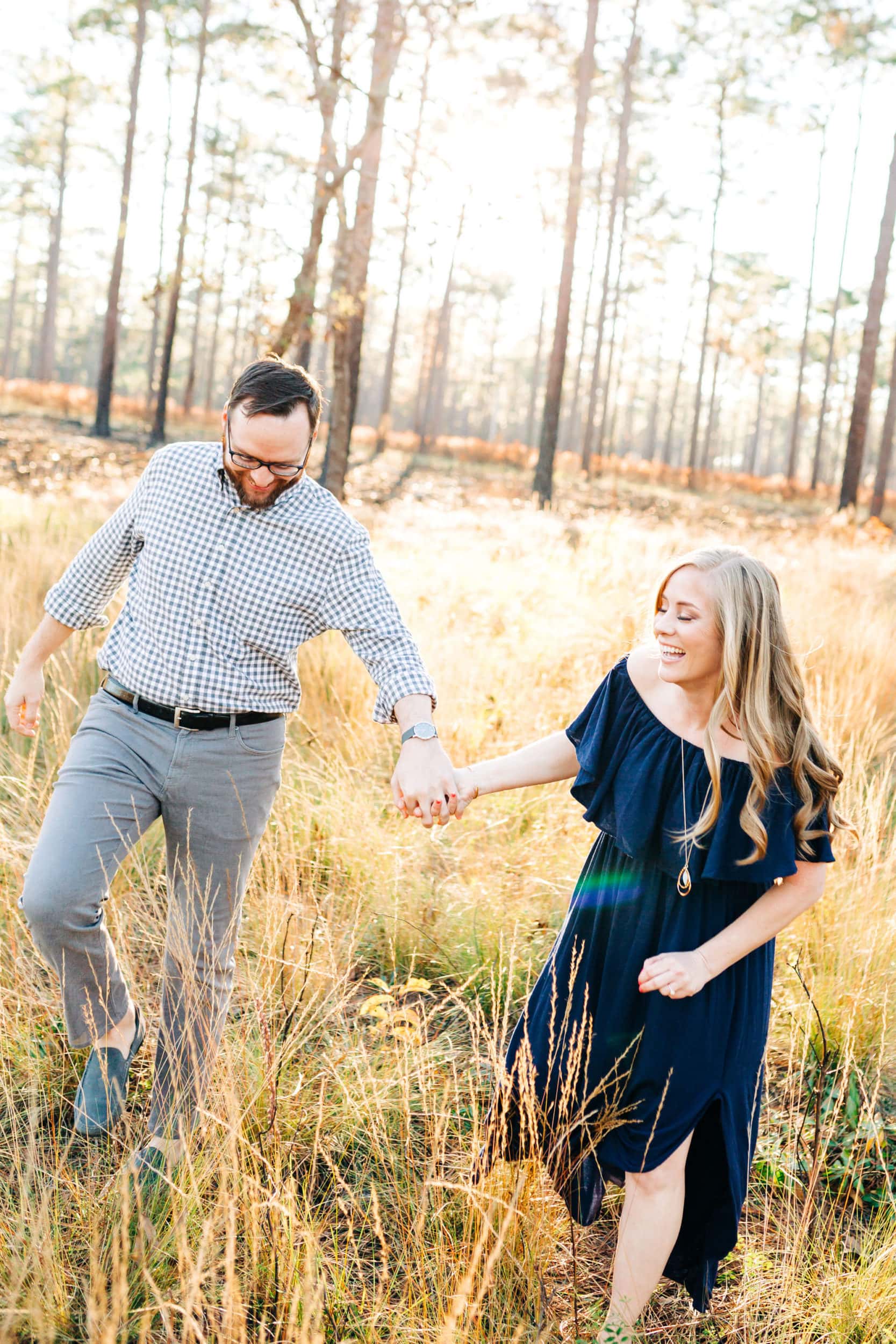 bride to be with navy dress holding hands with groom to be with grey shirt with field and woods in background at Wekiwa Springs State Park Engagement Session
