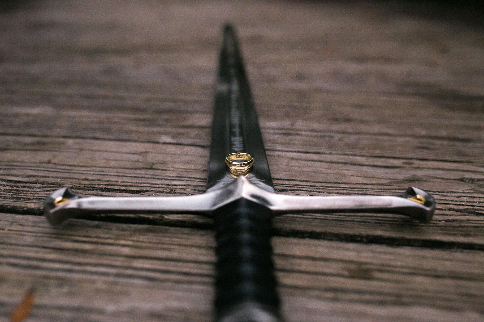 black sword with gold ring rested on top with wood in background at Wekiwa Springs Engagement Session