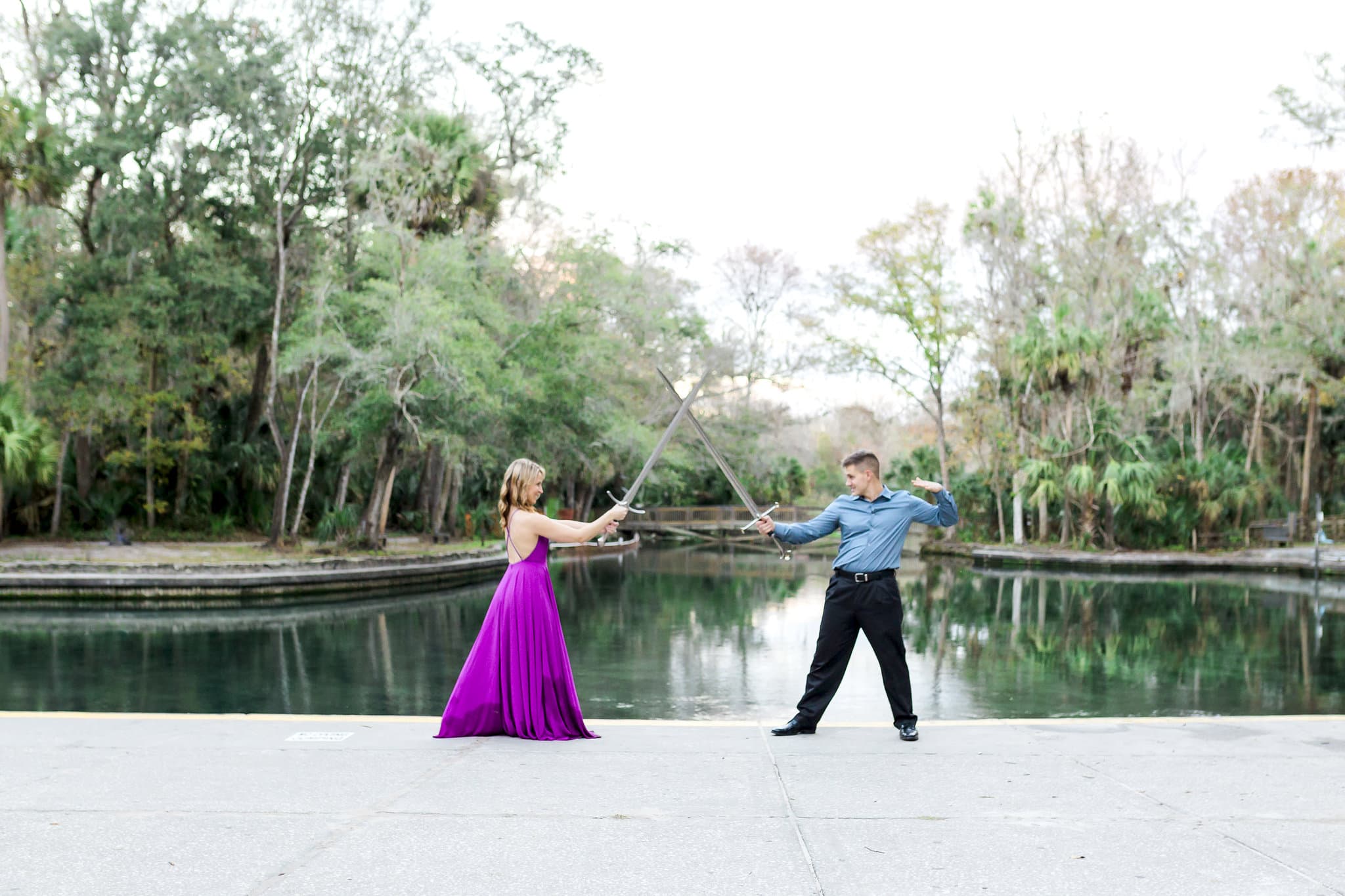 bride to be with flowy purple dress with groom with swords with pond in background at Wekiwa Springs Engagement Session