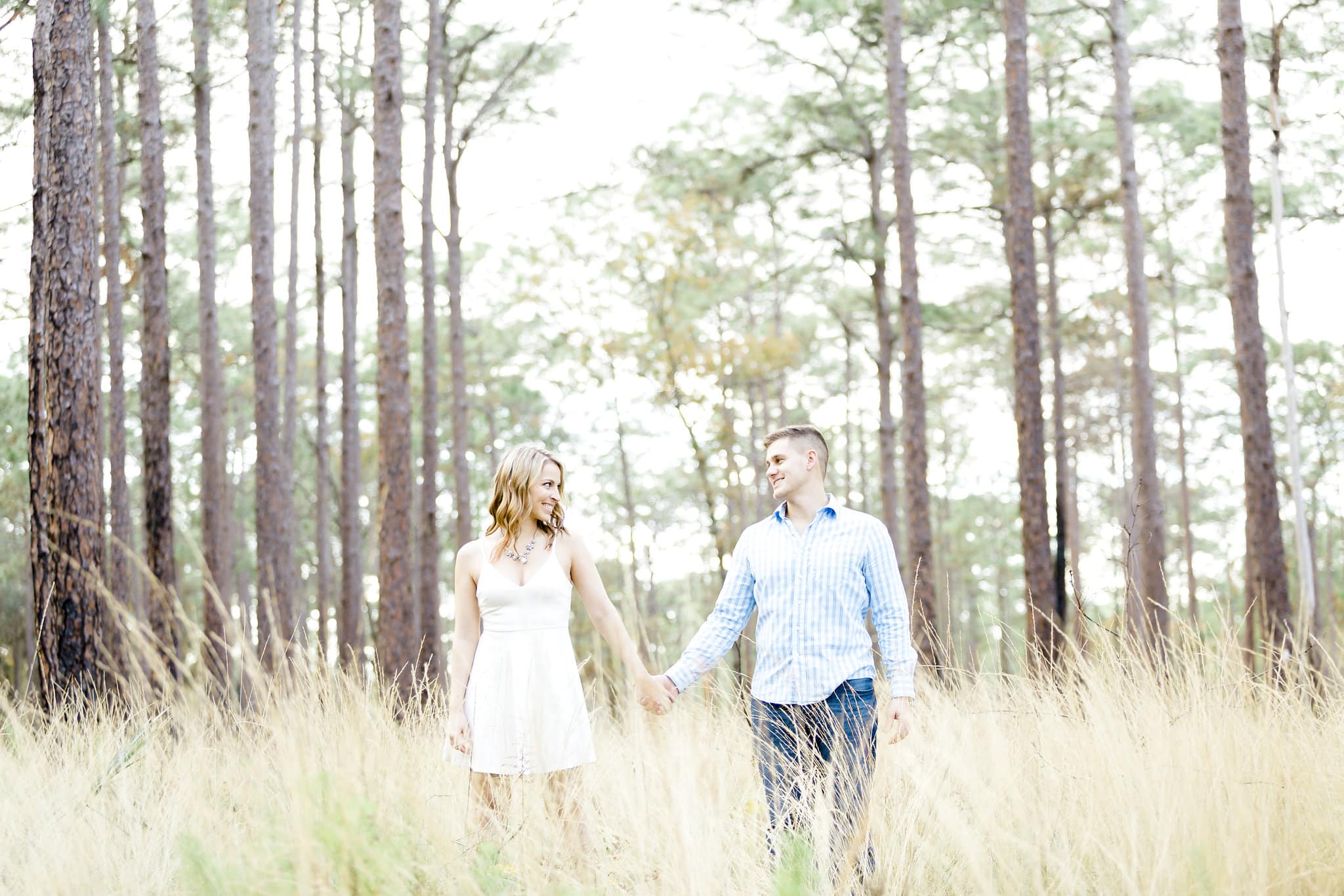 bride to be with white dress with groom to be with blue shirt with field and large trees in background at Wekiwa Springs Engagement Session
