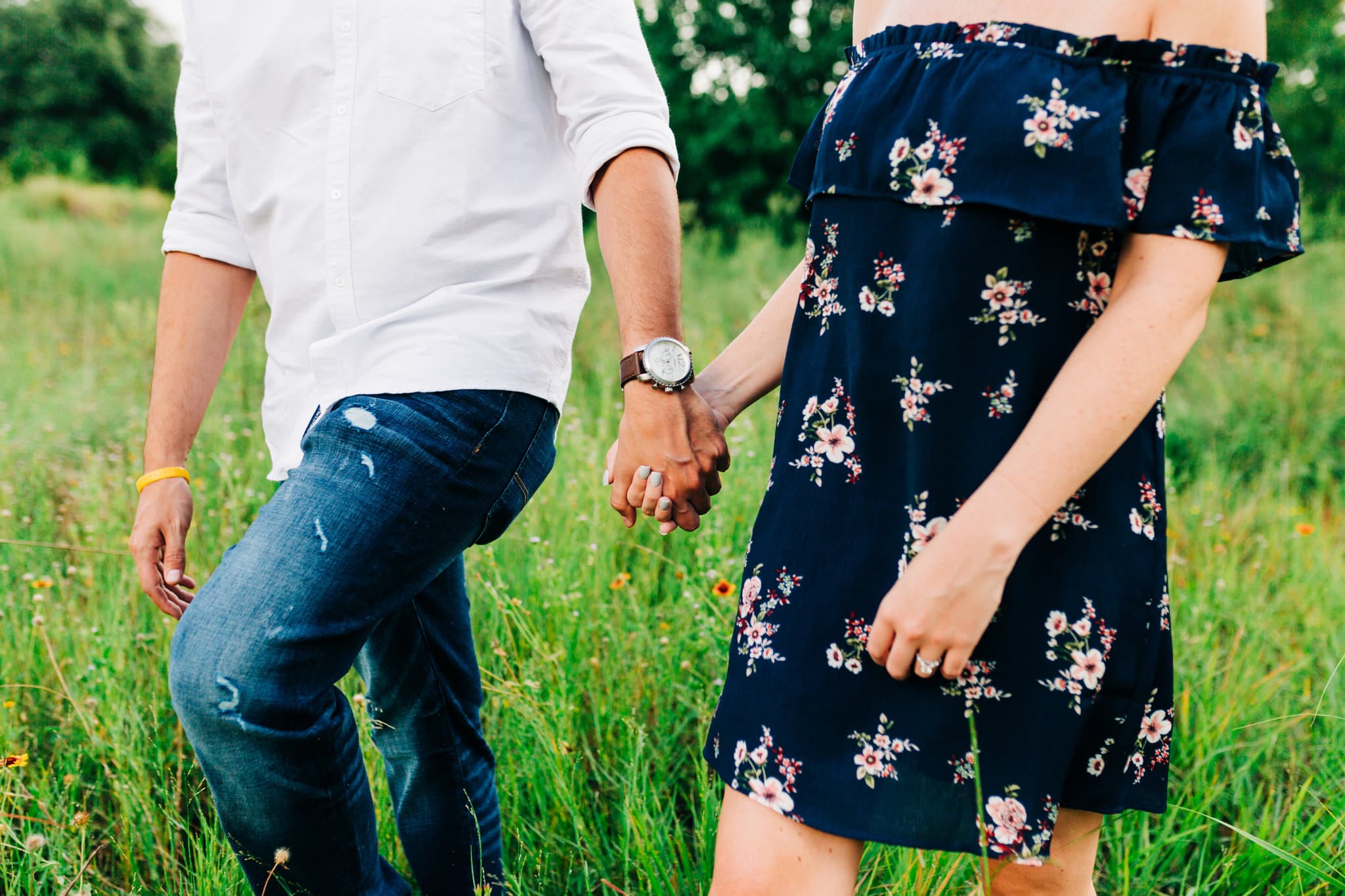 girl in blue floral strapless dress with guy with blue jeans with white button up shirt with watch with meadow in background at Baldwin Park Engagement Session