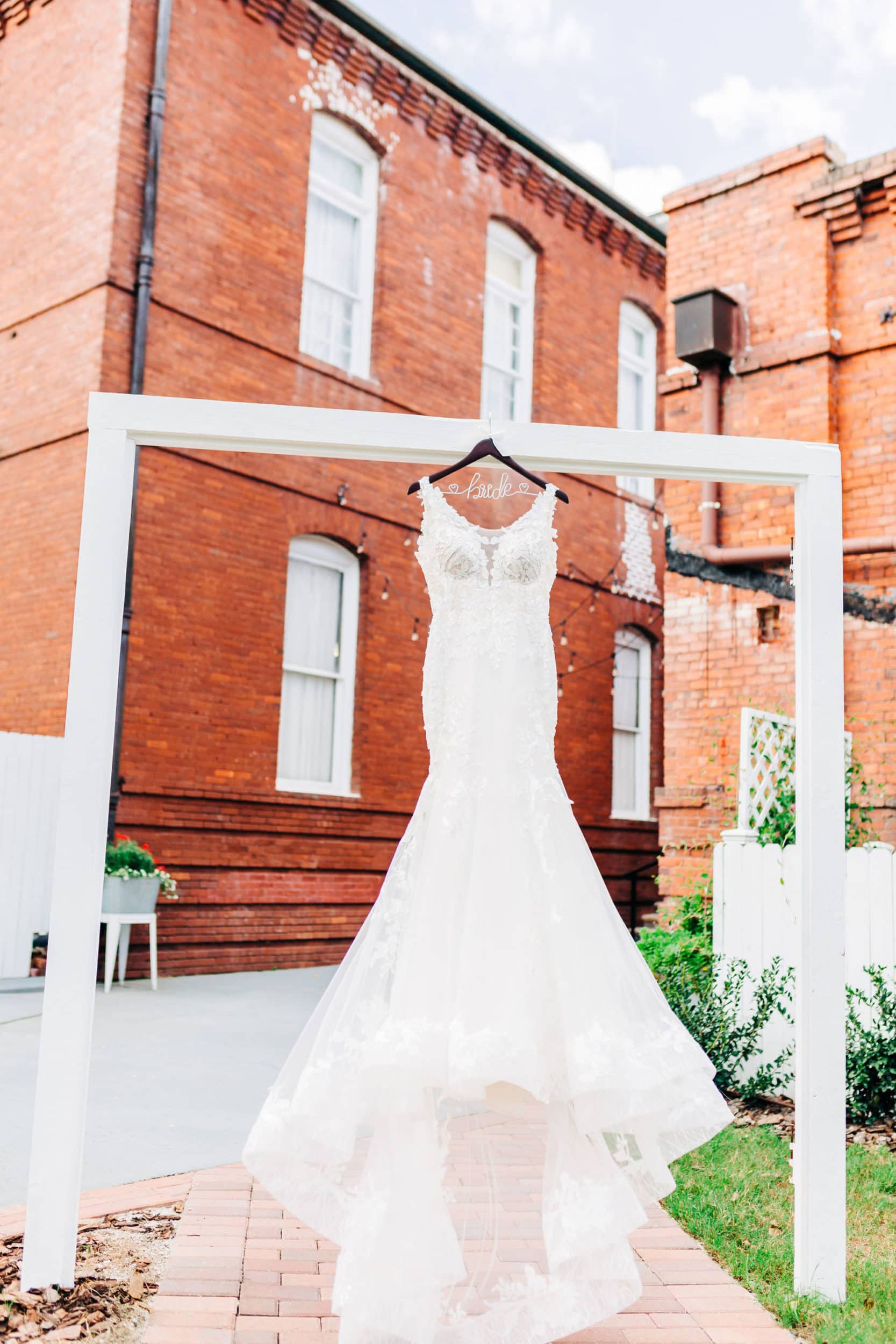 white bridal gown with white wood archway with large brick building with large white windows in background